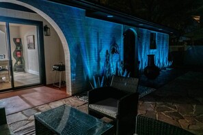 An outdoor patio with a glass door leading to a room, a wicker chair, and a stone floor. - Agave Azul Villa | Monthly/Weekly Discounted Rates (Clinton)
