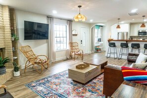 A living room with a sofa, chairs, a coffee table, and a TV. There is a kitchen area with bar stools and a refrigerator. - Agave Azul Villa | Monthly/Weekly Discounted Rates (Clinton)