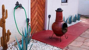 Un barbecue rouge est placé devant un bâtiment blanc, doté d’une porte en bois et d’une fenêtre.