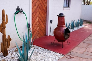 A red barbecue grill in front of a white building with a wooden door and a window.