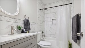 Un baño moderno con salpicadero de mármol, un lavamanos con una planta, un inodoro y una ducha con cortina.