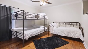 Un dormitorio con literas, ventilador de techo, alfombra negra y ventana con cortinas.