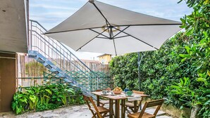 An outdoor patio with a table and chairs, a large umbrella, and a staircase leading to a higher level. - Nice apartment for 4 guests with A/C, WIFI, TV and balcony (Cecina)