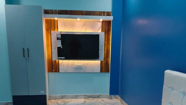 A bedroom with a bed, a TV mounted on the wall, and a wardrobe. - Viraj Homestay (Varanasi)