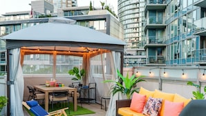 Eine Dachterrasse mit überdachter Sitzgruppe, einem Esstisch und einer Couch.