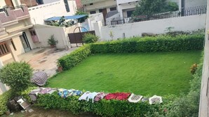 A residential area with a well-maintained lawn, a garden with various plants, and a row of houses in the background. - Hotel Pilgriims (Varanasi)