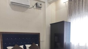 A bedroom with a bed, an air conditioning unit, a wardrobe, and a chair. - Hotel Pilgriims (Varanasi)
