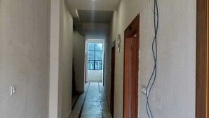 A hallway with a marble floor, white walls, and wooden doors. - Hotel Pilgriims (Varanasi)