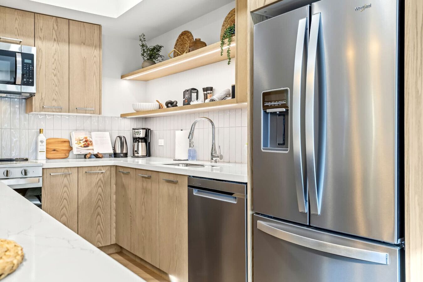 A modern kitchen with stainless steel appliances, wooden cabinets, and a white countertop.
