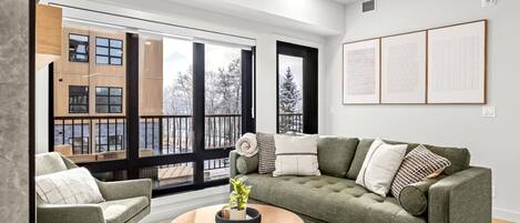 A modern living room with a green sofa, a round coffee table, and a view of a snowy outdoor balcony.