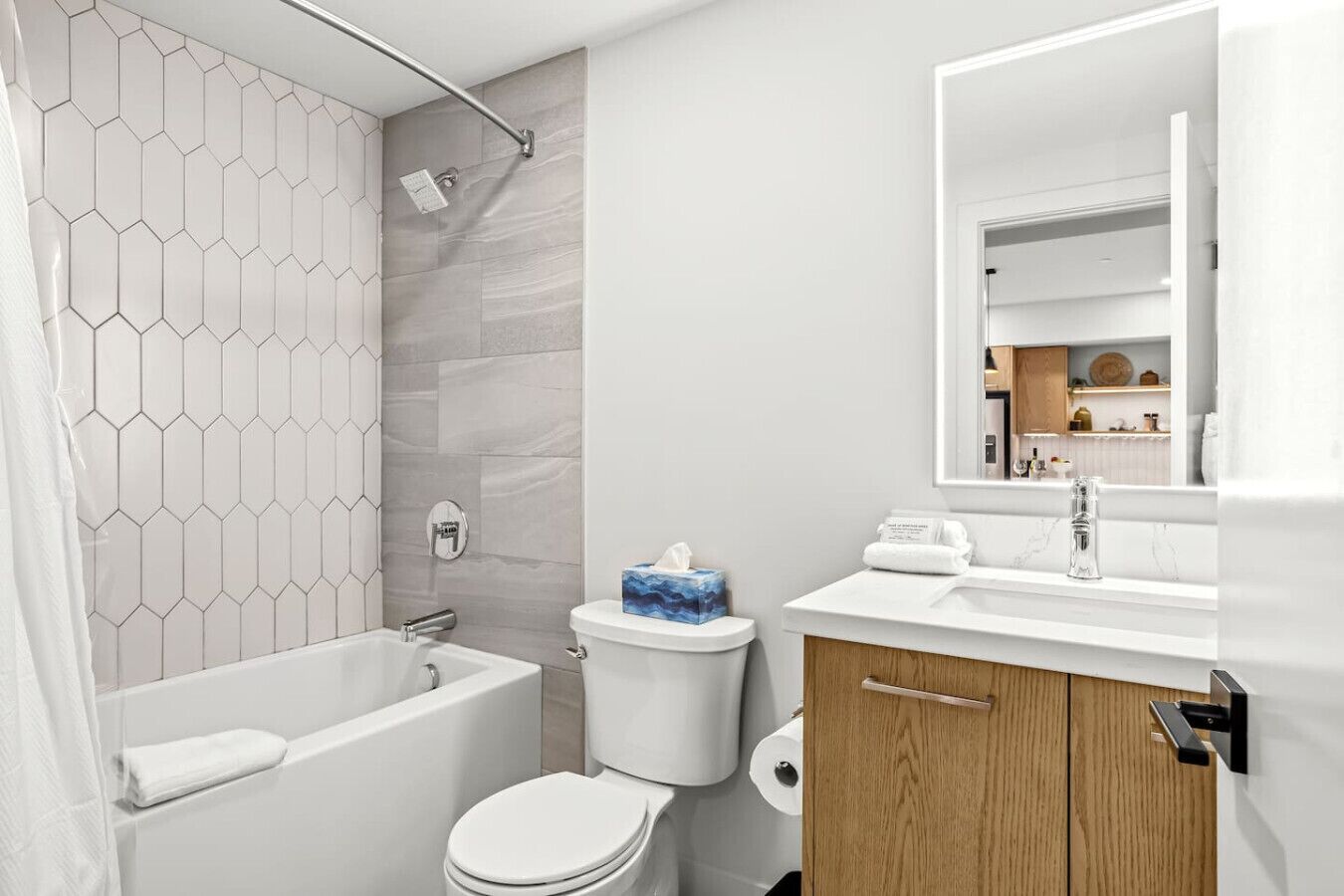 Et moderne badeværelse med en brusekabine med hexagonfliser, et hvidt toilet og en trævask med et spejl.