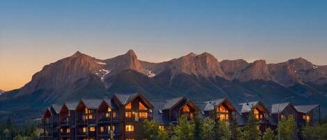 Un chalet composé de plusieurs bâtiments en bois, un parking et un paysage de montagne en toile de fond.