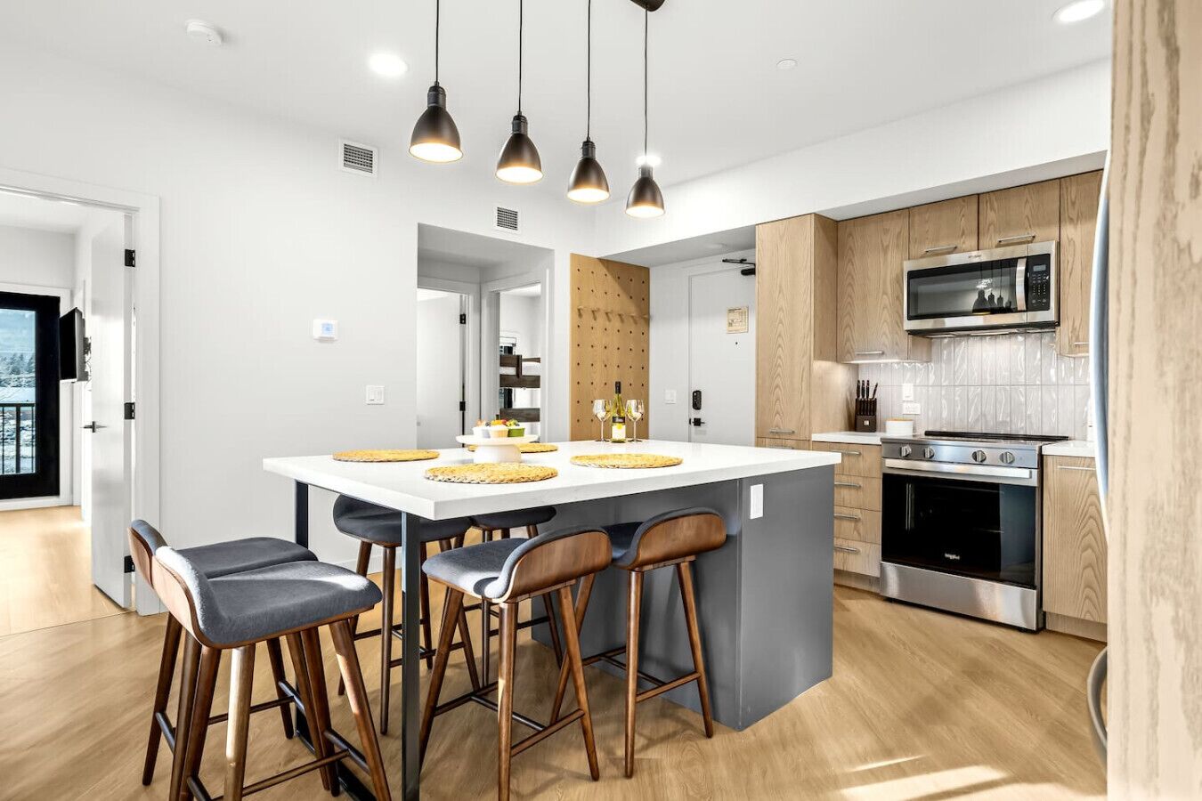 A modern kitchen with a central island, bar stools, a microwave, and an oven.