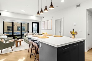 A modern kitchen with a large island, bar stools, and a dining area with a sofa and coffee table. - Modern Rocky MTN Stay, Sleeps 8 with Pool +and  HotTub! (Canmore)