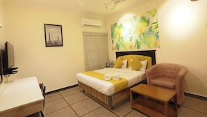 Una camera d'albergo con un letto, una scrivania, una sedia, un condizionatore d'aria, una ventola a soffitto e un quadro appeso al muro.
