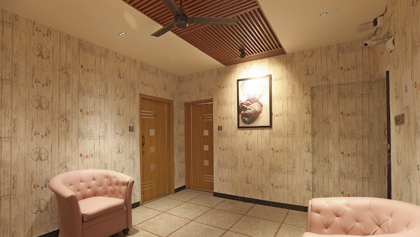 Camera d'albergo con soffitto in legno, due poltrone rivestite di rosa, un quadro appeso al muro e carta da parati decorata.
