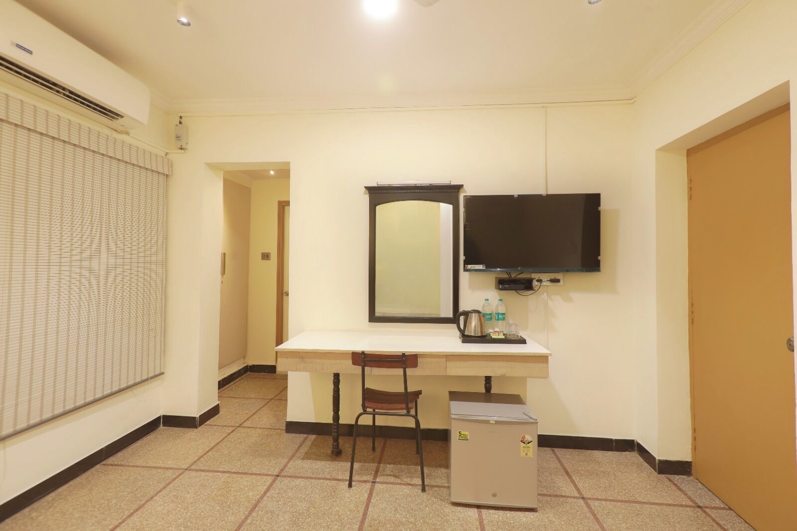 A hotel room with a desk, chair, and a small refrigerator.