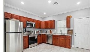 A modern kitchen with wooden cabinets, stainless steel appliances, and a white tiled floor.