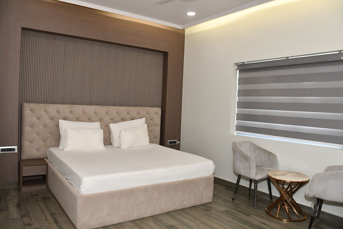 A modern bedroom with a large bed, a headboard, two bedside tables, a small round table, and a chair.