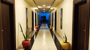 A hotel hallway with a black and white tiled floor, wooden doors on both sides, and potted plants along the corridor. - Shakti Resort (Behror)