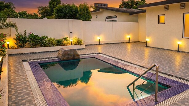 A rectangular swimming pool with a stone feature in the center, surrounded by a tiled deck. - Shakti Resort (Behror)