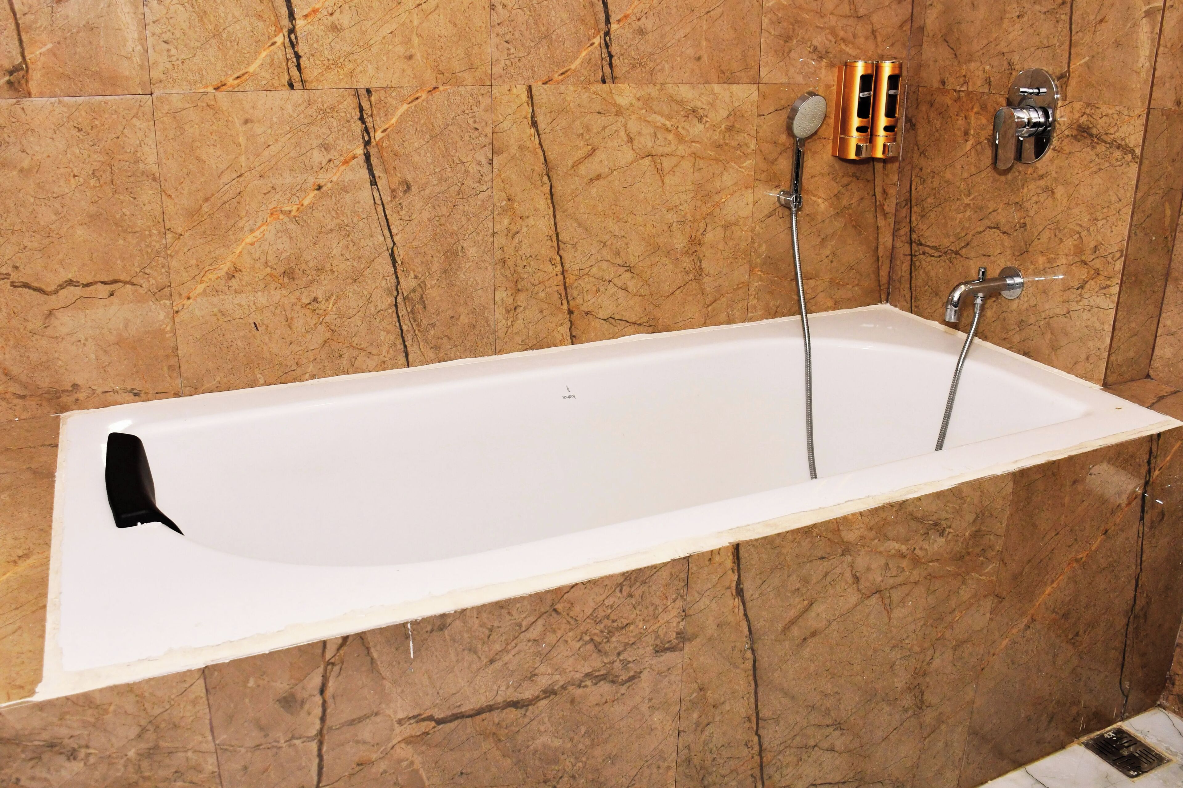 Una bañera blanca con grifo negro, frente a una pared de mármol.