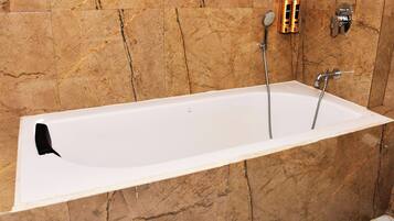 Una bañera blanca con grifo negro, frente a una pared de mármol.