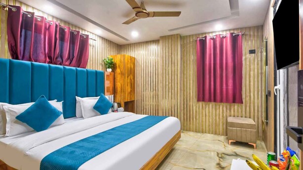 A modern hotel room with a large bed, a ceiling fan, and a small seating area. - Hotel Sona Deluxe @ 2Min From New Delhi Railway Station (New Delhi)