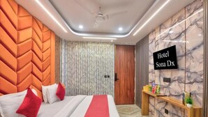 A hotel room with a bed, a TV, a wooden side table, and a marble wall. - Hotel Sona Deluxe @ 2Min From New Delhi Railway Station (New Delhi)