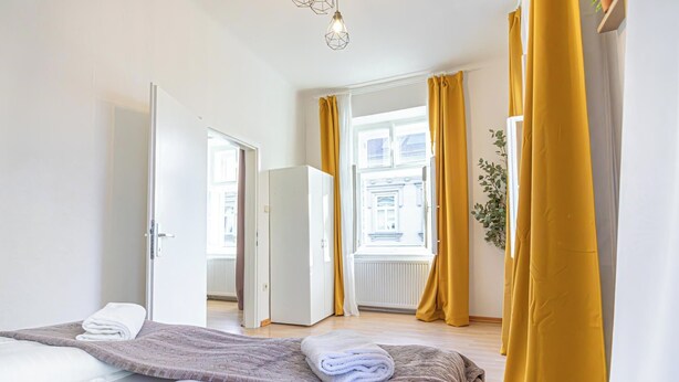 Een hotelkamer met een bed, een deur naar een andere kamer, een raam met gordijnen en een plant.