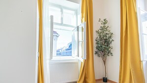 Een kamer met een raam, gele gordijnen, een potplant en een radiator.