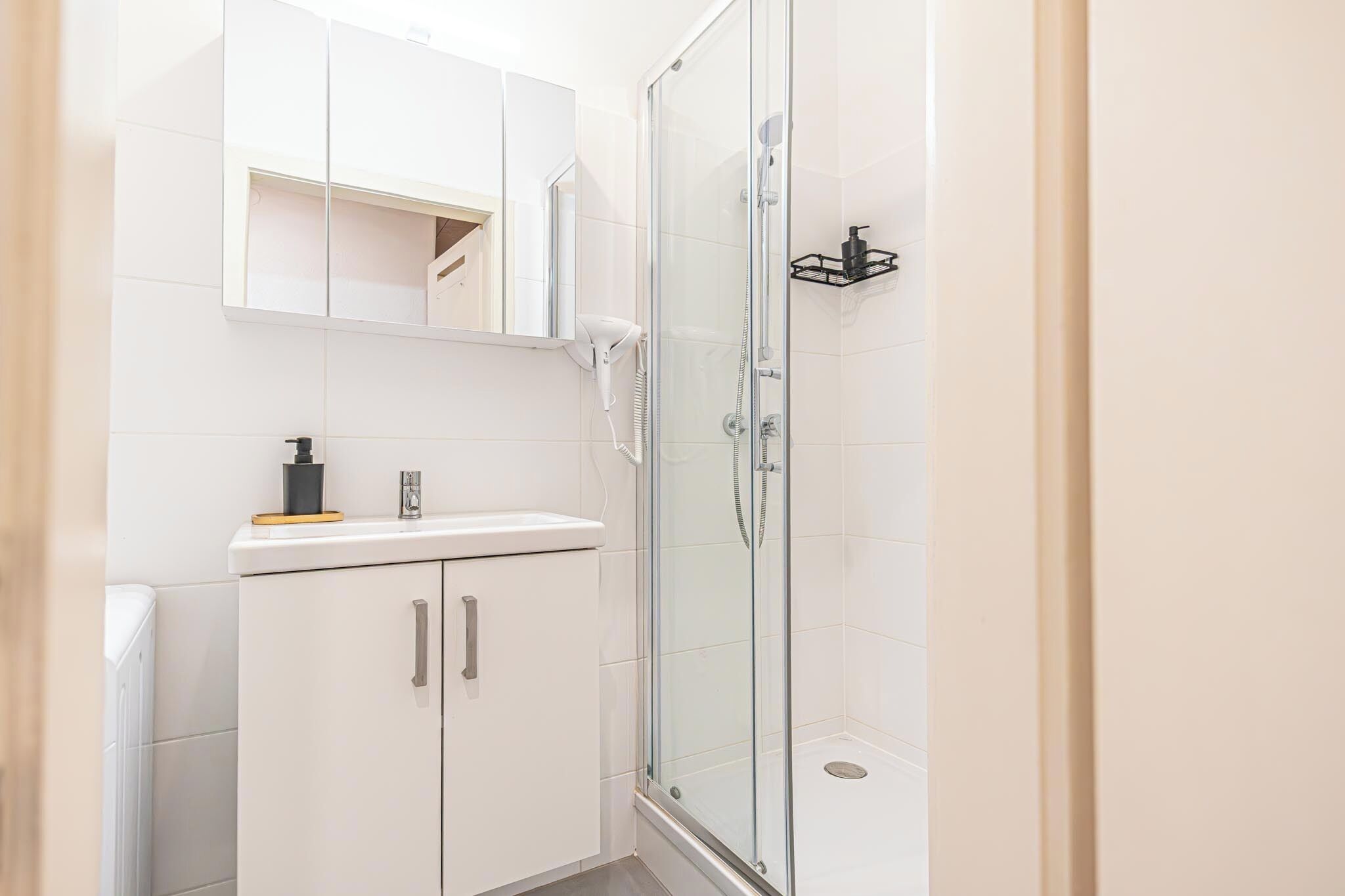 A modern bathroom with a glass-enclosed shower, a white sink, and a mirror above the countertop.