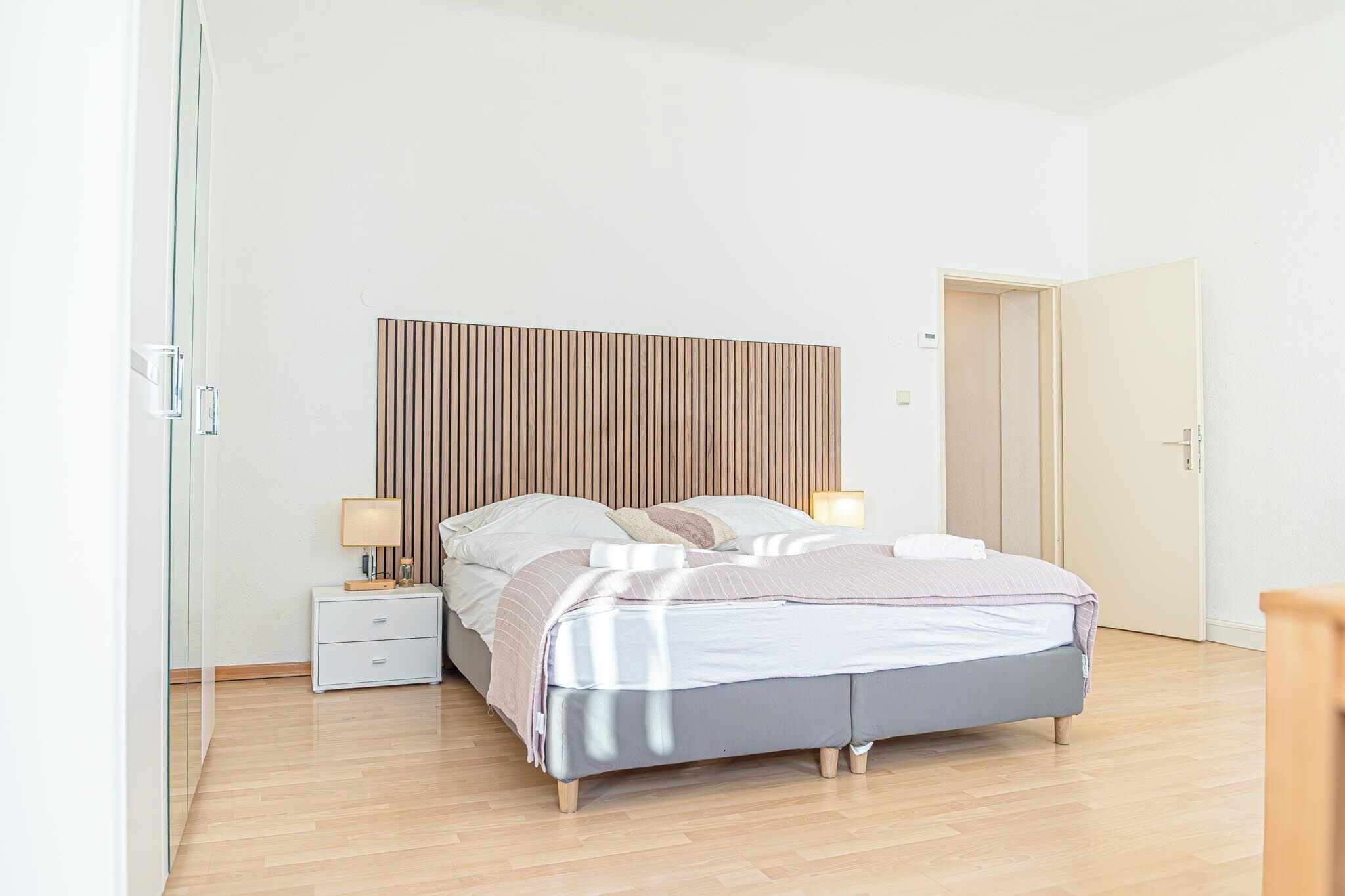 Ein modernes Schlafzimmer mit einem Bett, Nachttischen und einem Wandpaneel als Kopfteil.