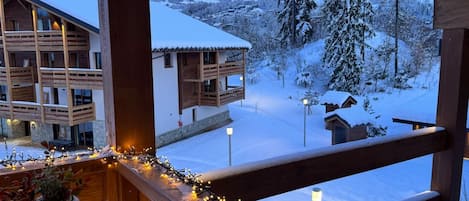 A wooden cabin with a balcony overlooking a snowy landscape and a mountain in the background.