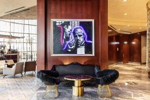 Eine Lobby mit Marmorboden, einem schwarzen Sofa mit goldfarbenen Füßen und einem gerahmten Kunstwerk an der Wand.