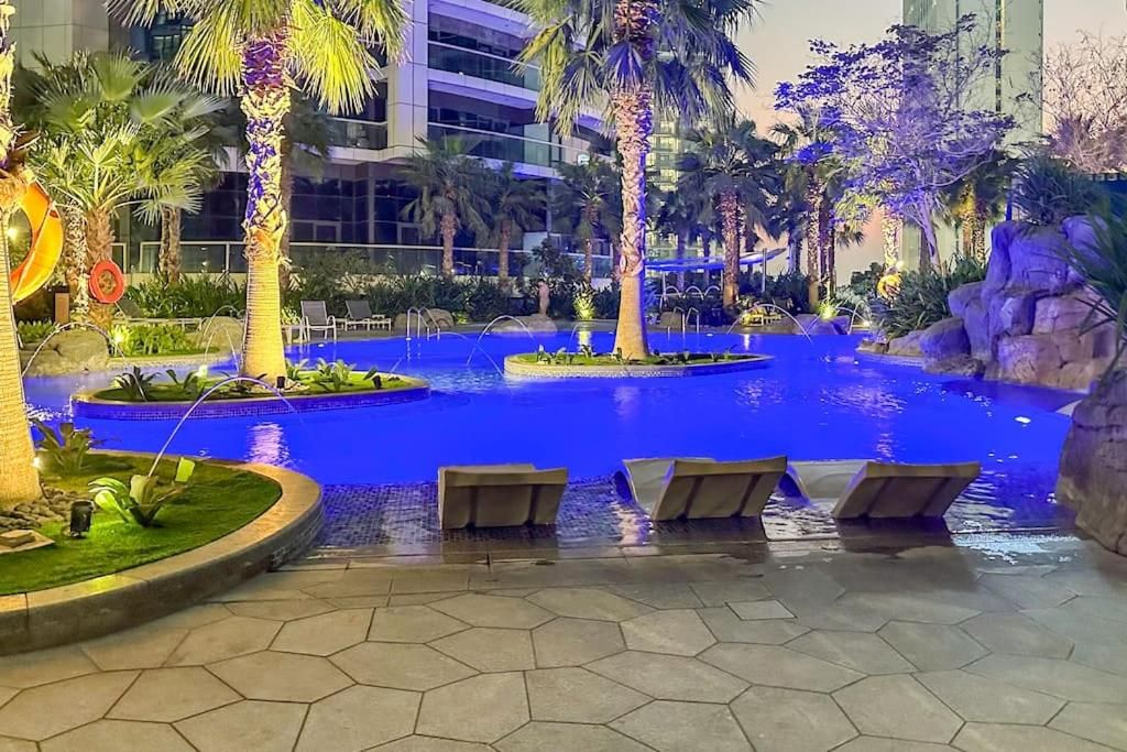 Un espace piscine aménagé avec des chaises longues, des palmiers et un élément décoratif aquatique.
