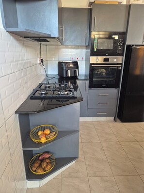 A modern kitchen with a gas stove, a coffee maker, a microwave, and an oven. - Luxury Mombasa Apartment with Ocean and City Views (Mombasa)