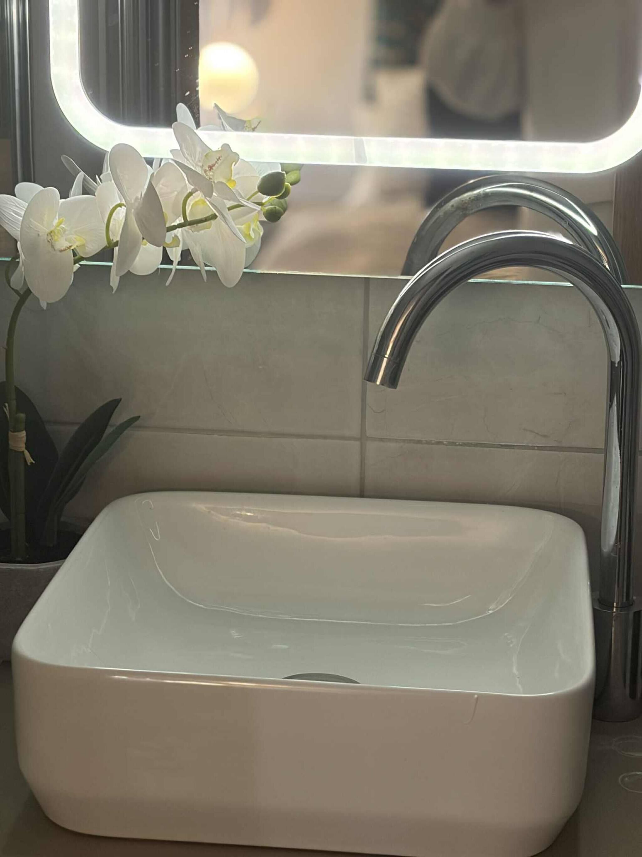 A bathroom with a rectangular white sink, a chrome faucet, and a mirror above it.