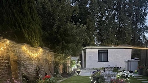 A well-maintained patio area with a tiled floor, surrounded by lush greenery and decorative lighting. - Wonky 2– A Cosy Hideaway in the Heart of Cheshire (Macclesfield)