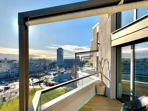 Un apartamento moderno con balcón que ofrece vistas a un paisaje urbano, destacando un edificio alto y una glorieta.