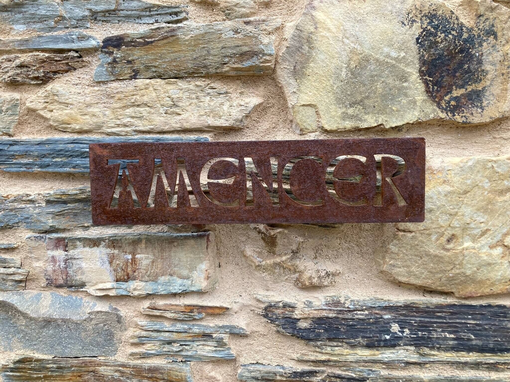 A metal sign with the name "MANCER" mounted on a stone wall.