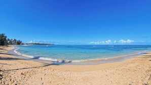 A beach with clear blue water, sandy shore, and a distant shoreline with buildings and trees. - 2BR Beachfront Apt Las Terrenas - La Dolce Vita 9 (Las Terrenas)