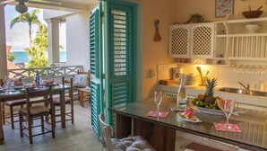 A kitchen with a dining area, a view of the ocean, and a teal door. - 2BR Beachfront Apt Las Terrenas - La Dolce Vita 9 (Las Terrenas)