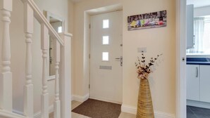 A hallway with a white door, a brown doormat, and a vase with flowers. - Modern Cambridge Home Business & Holiday Stays (Cambridge)