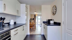 A modern kitchen with white cabinets, a black countertop, and a dining area with a wooden table and chairs. - Modern Cambridge Home Business & Holiday Stays (Cambridge)