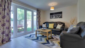 A living room with a sofa, a coffee table, and a large window with curtains. - Modern Cambridge Home Business & Holiday Stays (Cambridge)