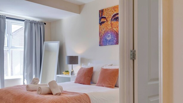 A bedroom with a bed, pillows, a bedside table, a lamp, and a painting on the wall. - Modern Cambridge Home Business & Holiday Stays (Cambridge)
