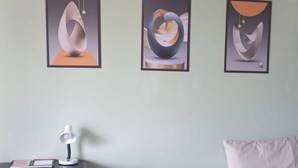 Una habitación con escritorio, una silla, una cama y tres cuadros abstractos en la pared.