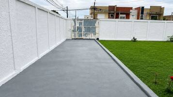 A concrete pathway leading to a gated entrance, surrounded by a white wall and a grassy area.