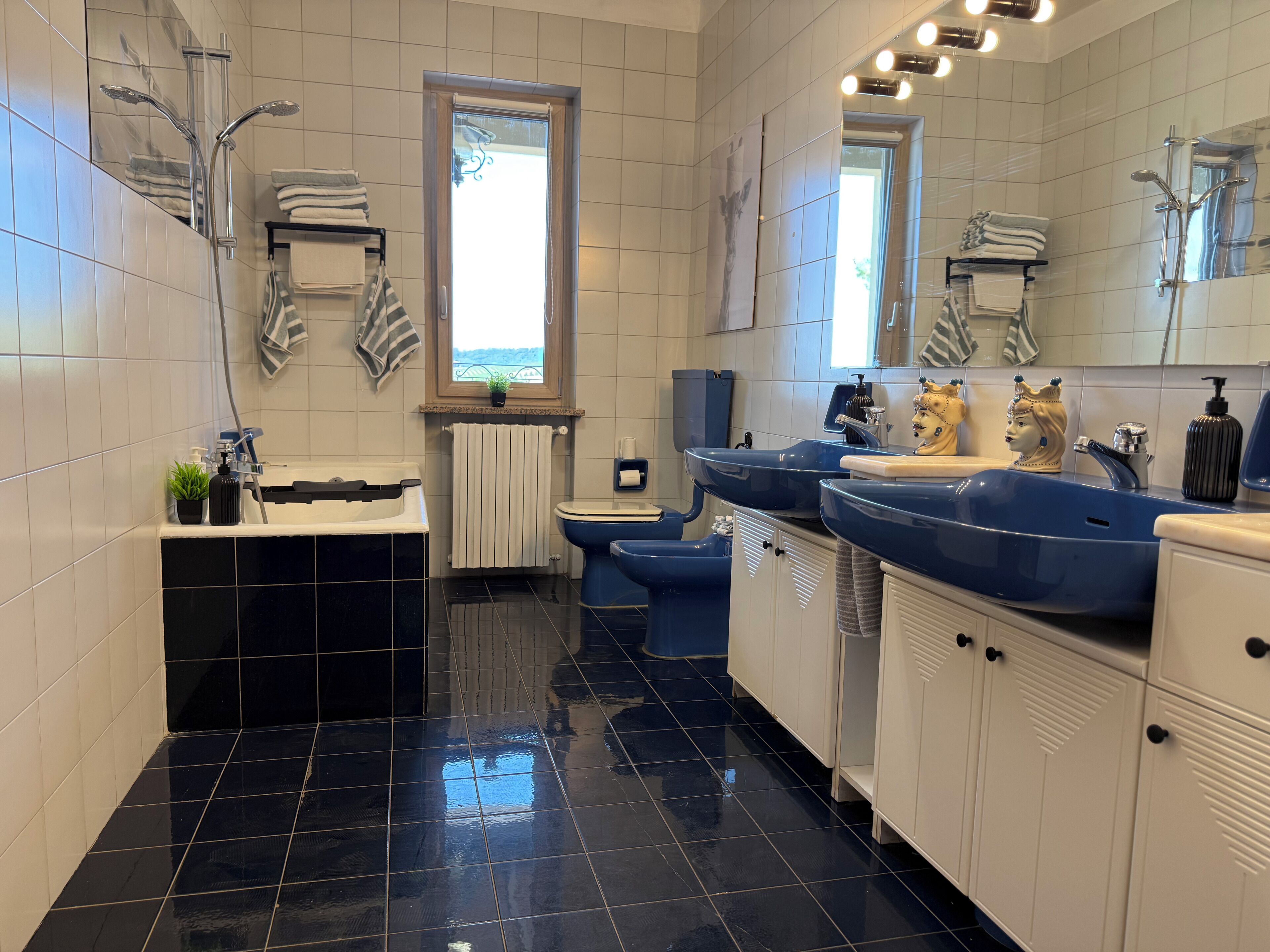A modern bathroom with a black tiled floor, a white toilet, a blue sink, and a shower area.